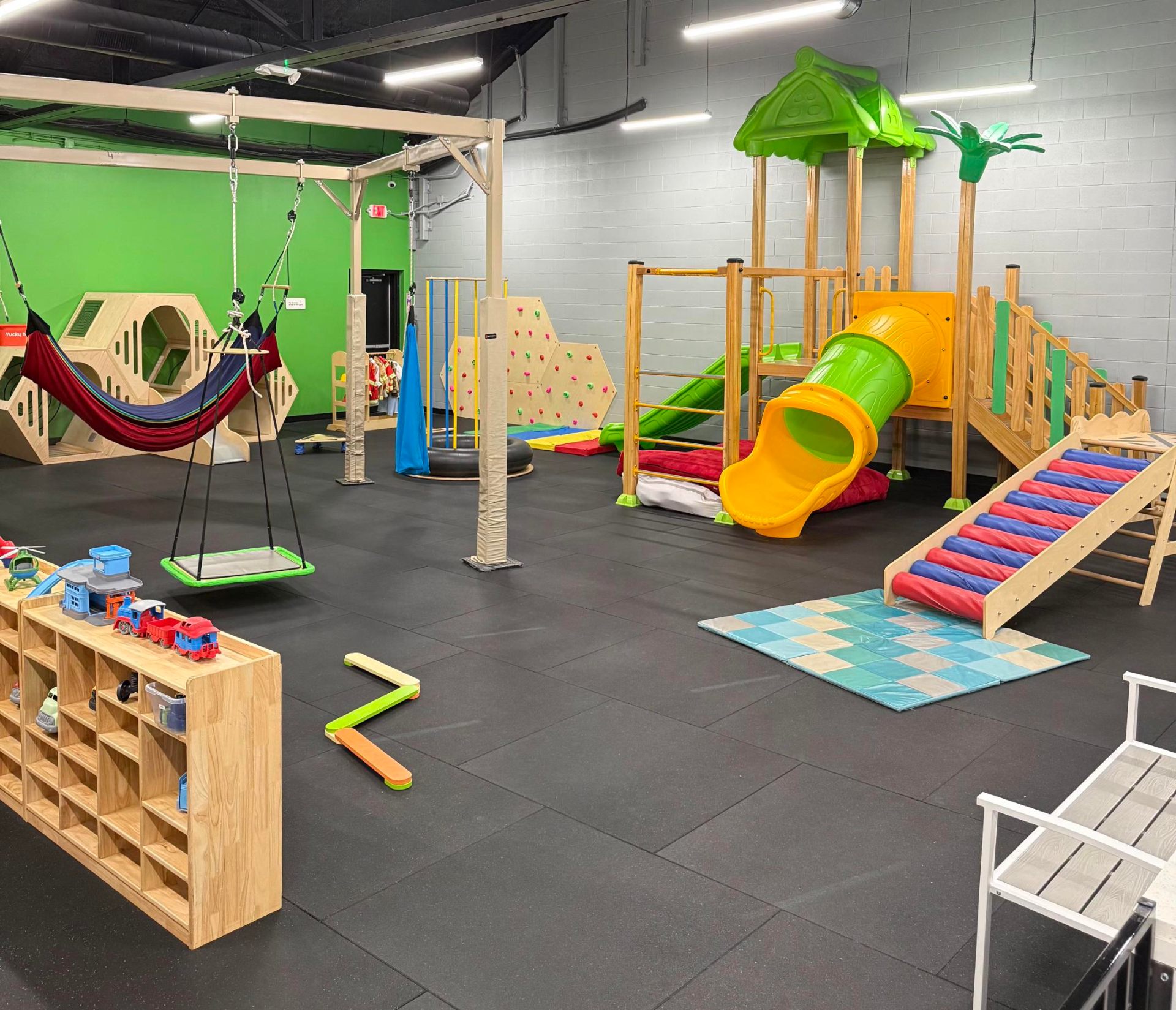 Wide view of the New Braunfels sensory gym with hammock swing, climbing wall, slide, and tunnel play structure