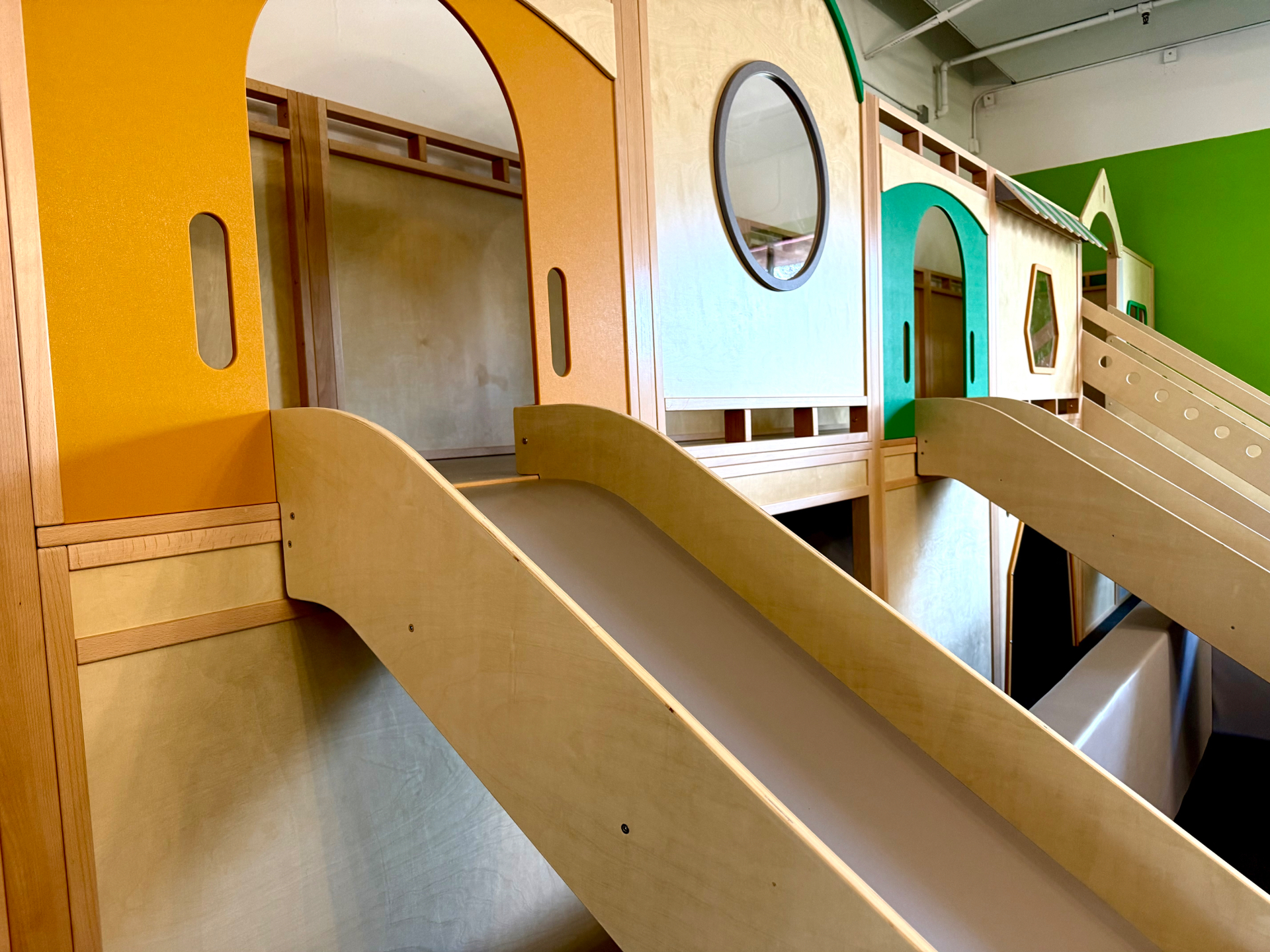 Twin wooden slides descending from the colorful arched play structure at Little Land Arcadia