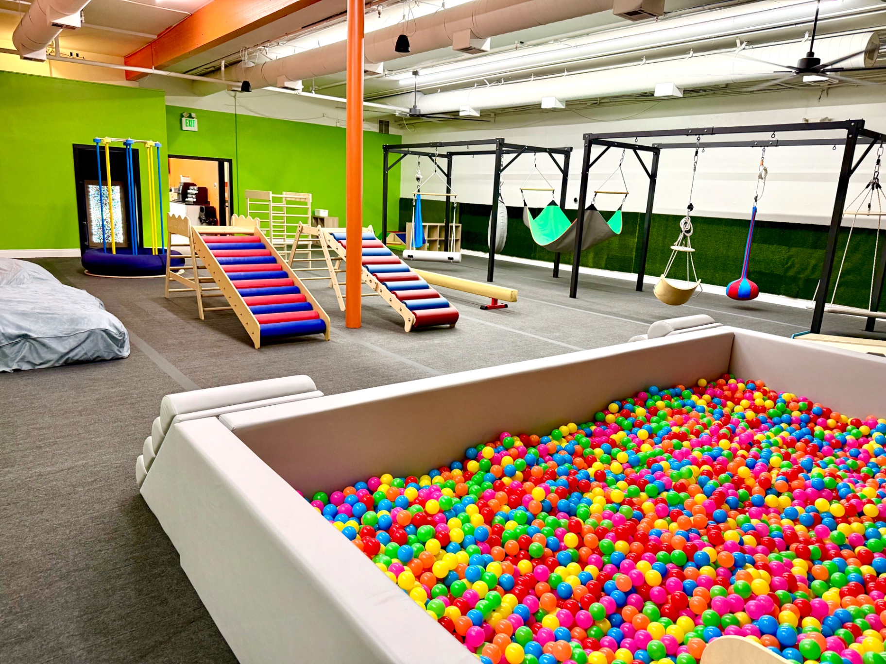 Open sensory gym at Little Land Arcadia with ball pit, climbing ramps, and suspended swings