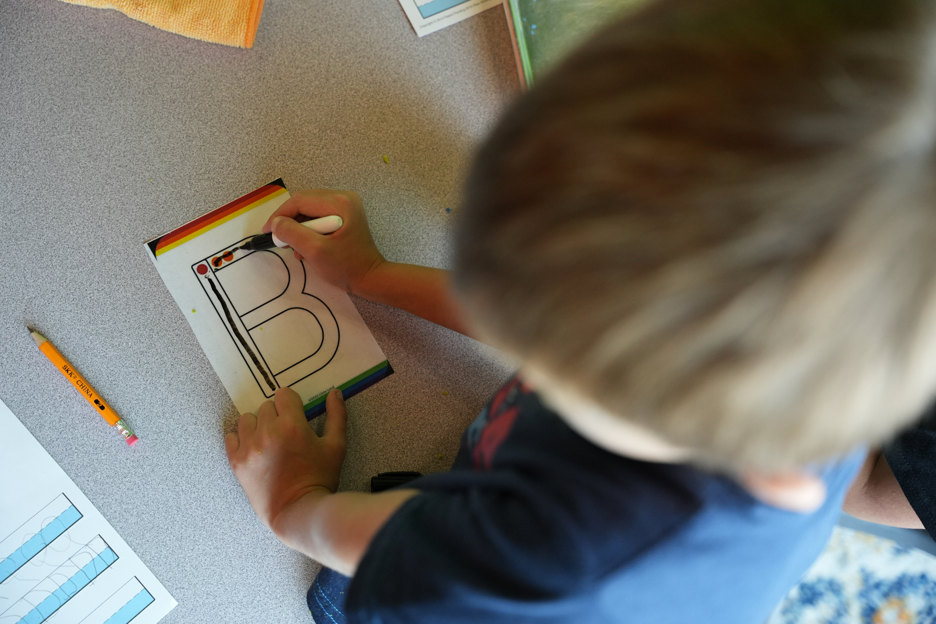 Overhead view of a child tracing the letter B on a Little Land worksheet