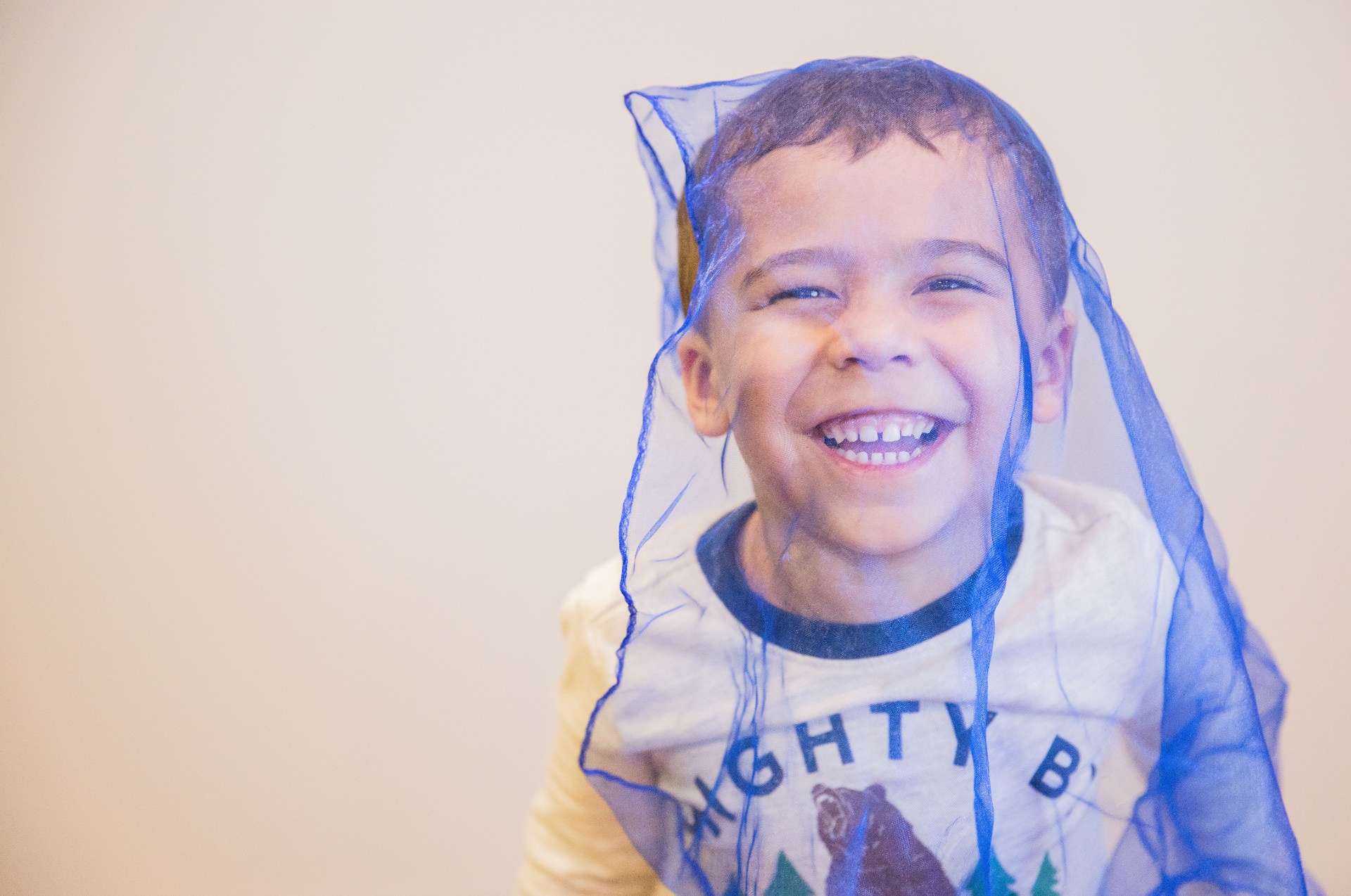 Boy giggling under a blue play scarf in Music Exploration
