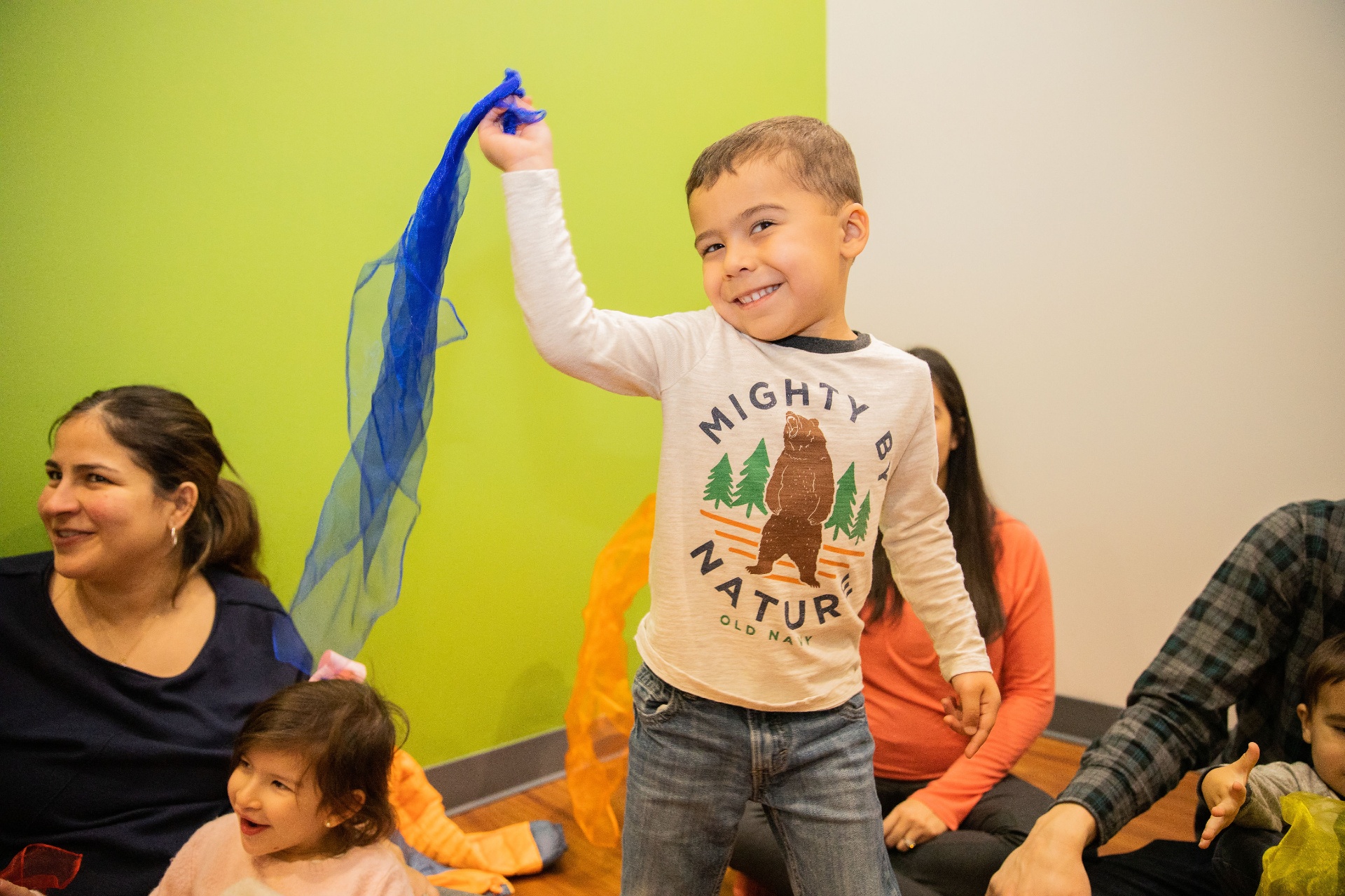 Toddler tossing a blue scarf in the air during caregiver-and-child music class