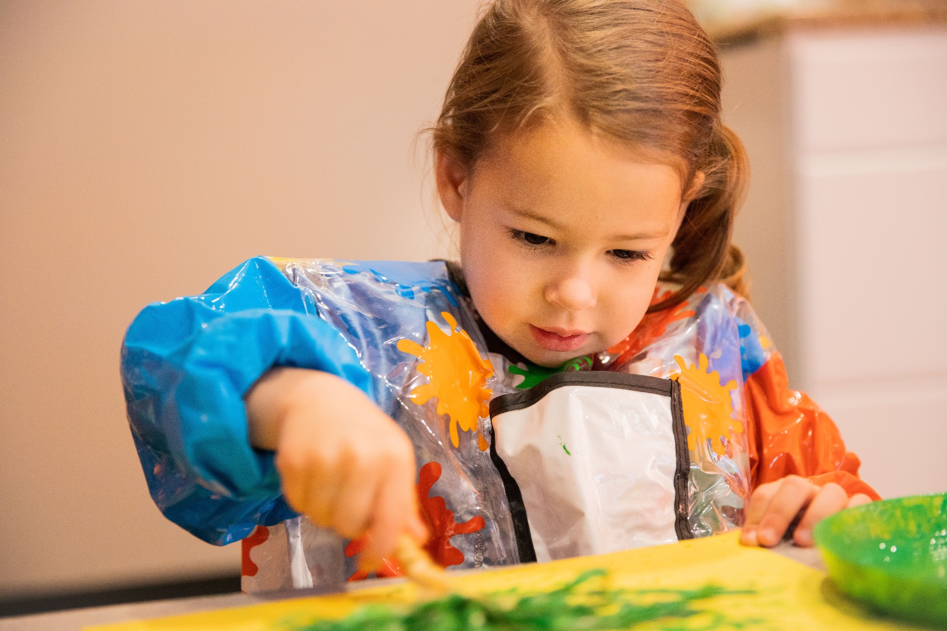 A child concentrating while finger painting in green and yellow