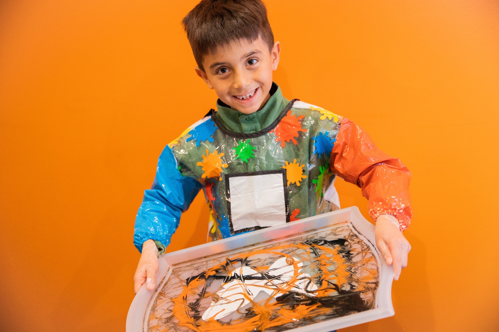 A child proudly holds a marbled paint tray made in Sensory Art class